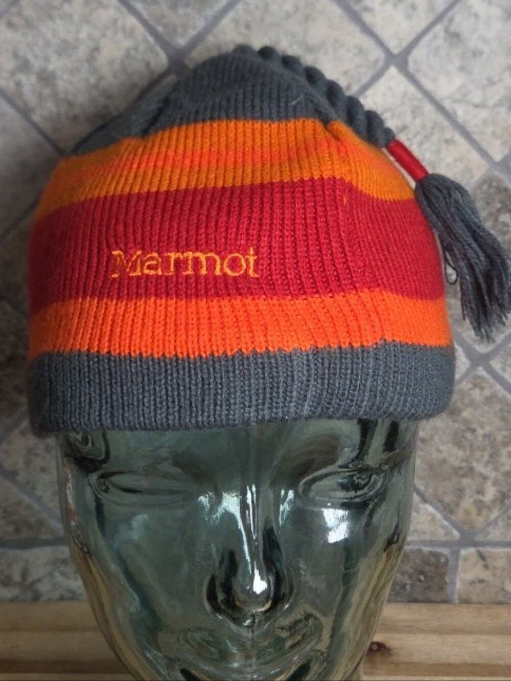 Striped Marmot knit beanie featuring gray, orange, and red bands W/ Tassel